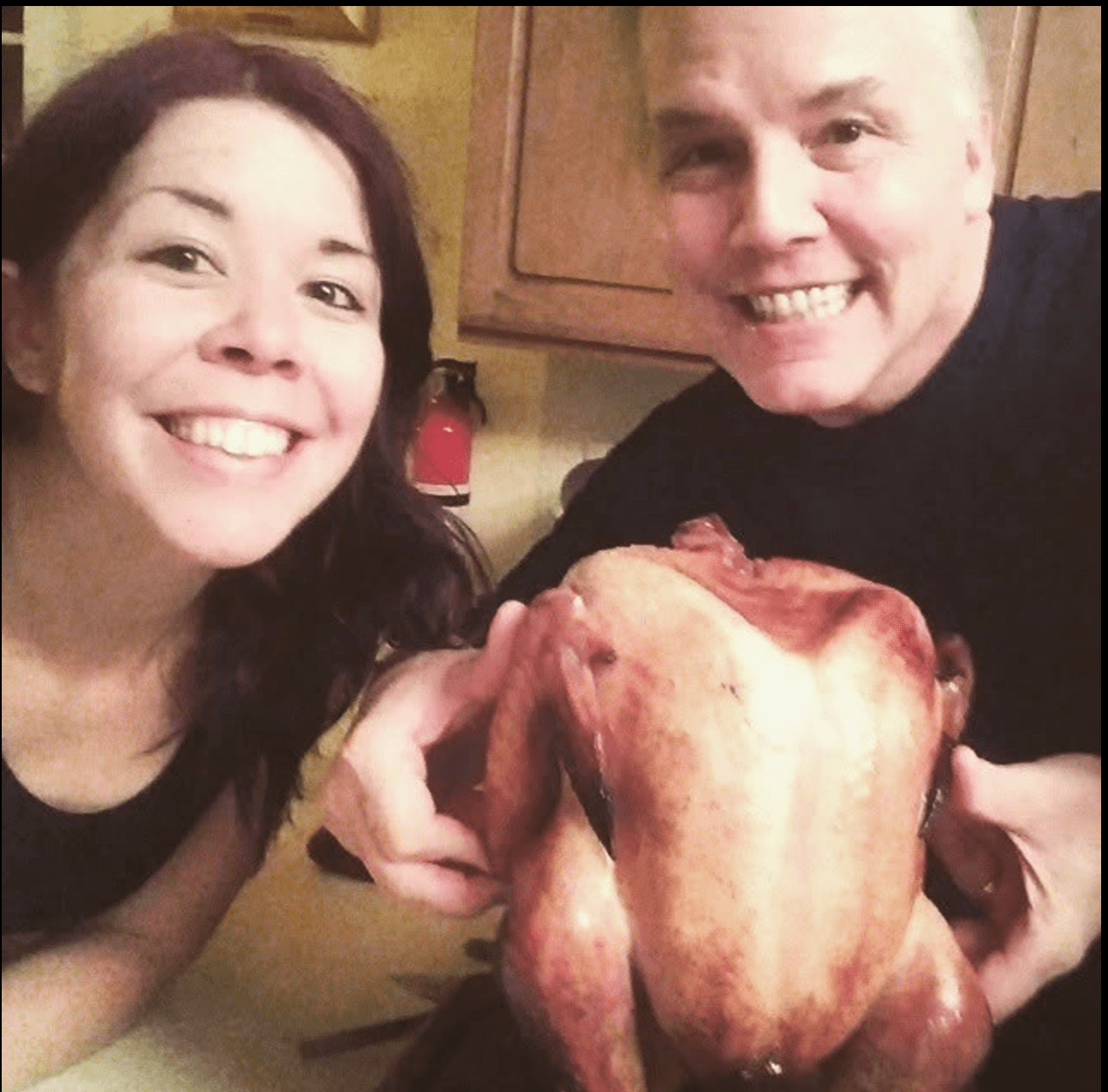 Rachael and her dad smiling in the kitchen, holding a roasted turkey.